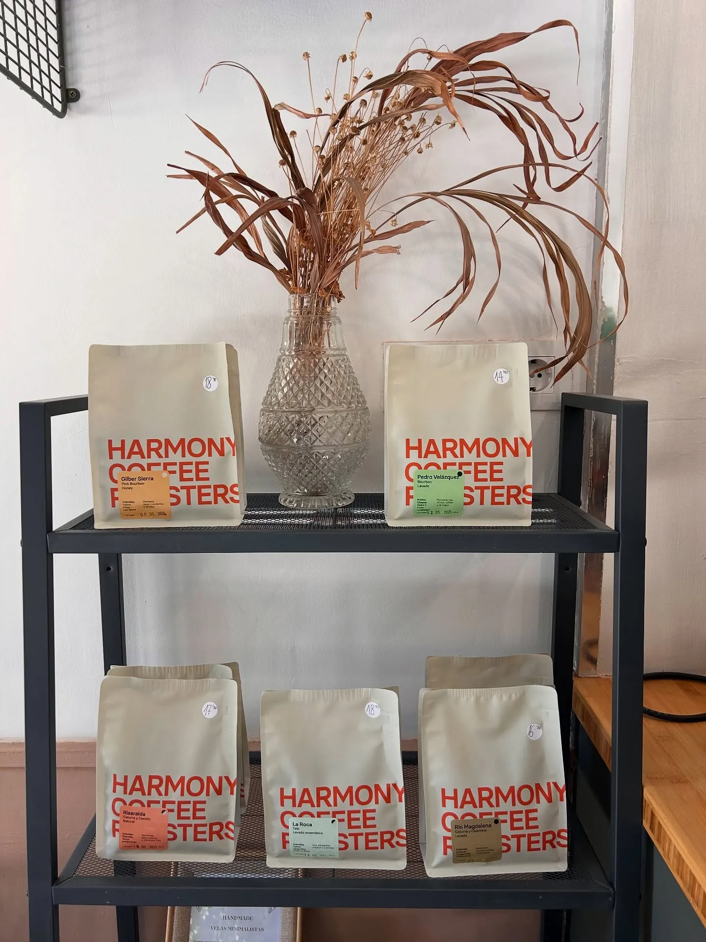 Estantería con bolsas de café y un jarrón con flores secas