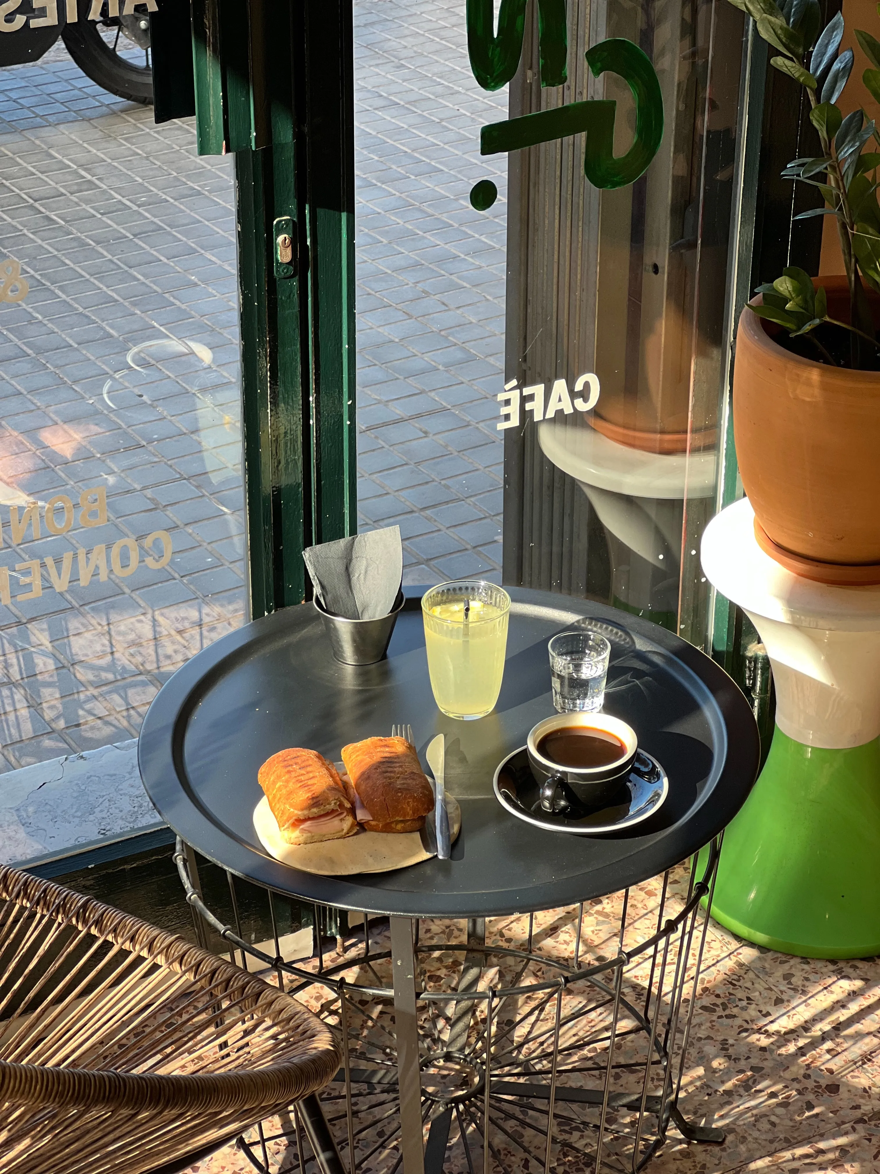 Mesa al sol junto a la puerta con un café, algo de comer y una limonada