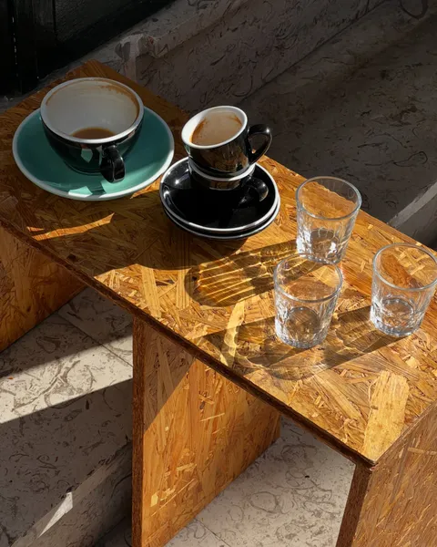 Tazas de café vacías y vasos de agua sobre un banco de madera al sol
