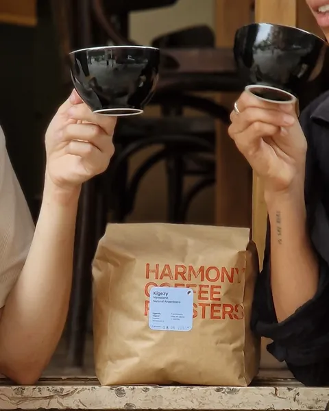 Dos personas brindan con tazas negras junto a una bolsa de café