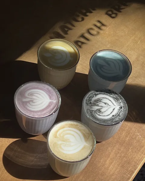 Cinco lattes de colores con arte latte sobre una mesa de madera al sol